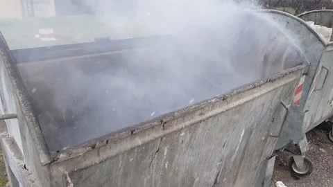 Garbage container set on fire, gray smoke coming out of it Stock Footage 231689589