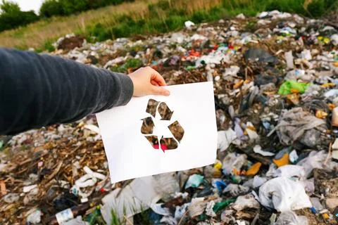 Garbage pollution. Hand holding cut paper with the logo of recycling on dum.. Stock-Fotos