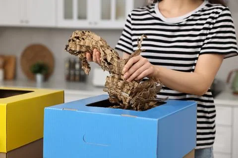 Garbage sorting. Woman throwing shredded paper into cardboard box in kitche.. Stock Photos