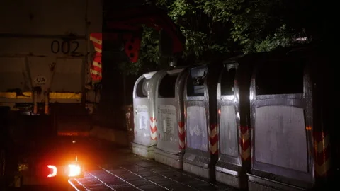 A garbage truck is lifting a trash container in the rain during the dark hours Stock Footage 278933057