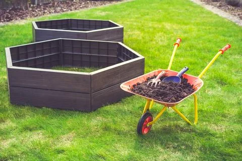 Garden barrow with soil and empty raised beds on grass prepared for fillin... Stock Photos