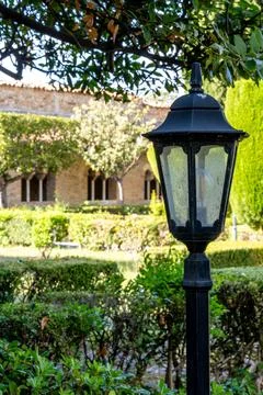 Garden lantern under tree branches with arched building Photos