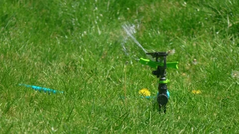 Garden sprinkler reducing water stream and turning off on fresh grass with Stockbeeldmateriaal 338389294