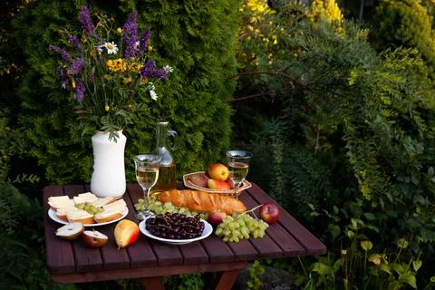 Garden table setting with wine, cheese, and fruits for a relaxing evening Stock Photos