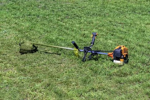 Garden trimer with a gasoline engine on the background of summer grass. Stock Photos