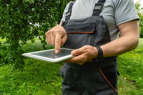 A gardener dressed in work clothes stands outdoors in a green area. They ar.. Stock Photos