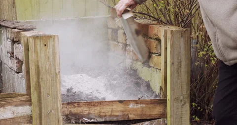 Gardener emptying the tray containing ash from wood burner on to a compost heap Stock Footage 149788074