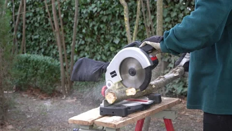 Gardener in  gloves cuts small logs with electric miter saw Practyl. Close-up. Stock Footage 166507002