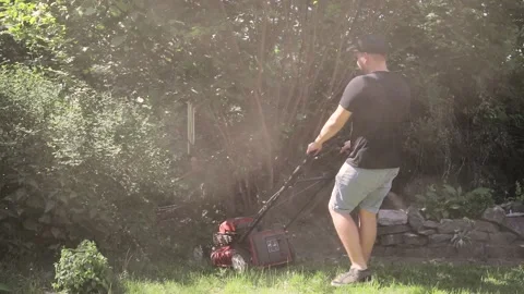 Gardener mowing the grass in the backyard. bright sunbeams and dust Stock Footage 131618451