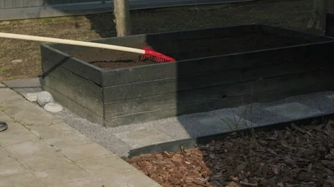 Gardener preparing soil in a raised garden bed with a rake for planting Stock Footage 331474676