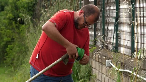 Gardener replacing trimmer line on grass cutter during outdoor work Stock Footage 333194480
