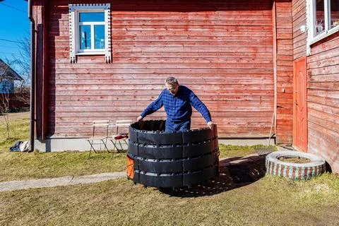 Gardener setting up compost bin by connecting plastic sections outdoors. Stock Photos