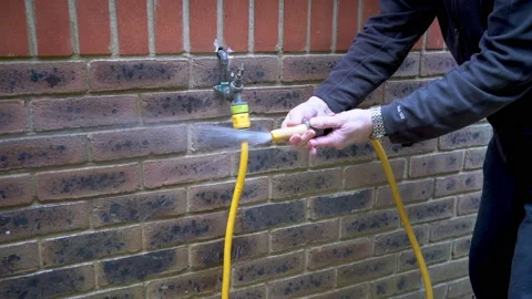 Gardener setting up the pressure on an outside cold water tap with hosepipe atta Vidéo 163102643