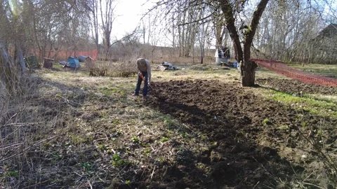 Gardening in the spring time at a field with trees in the background Vídeos de archivo 332065183