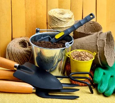 Gardening tools, peat cups, thread; seeds in tins against wooden fence Stock Photos