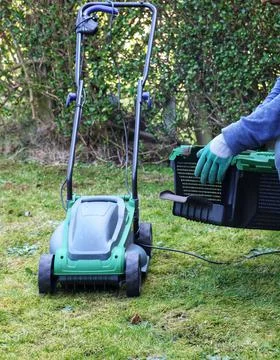 A gardner attaching empty grass basket to electric lawn mower machine Foto stock
