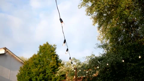 Garland of light bulbs glows against the background of the sky and green trees Stock Footage 160410341