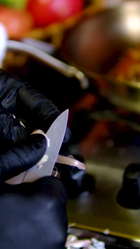 Garlic peeled with kitchen knife by chef wearing black gloves beside hot stove Video stock 346181507