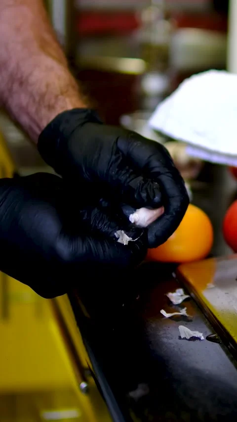 Garlic peeled with kitchen knife by chef wearing black gloves beside hot stove Video stock 346181578