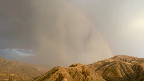 Garni Mountains landscape with dramatic clouds and rainbow arching over rugged Stock Footage 344516255