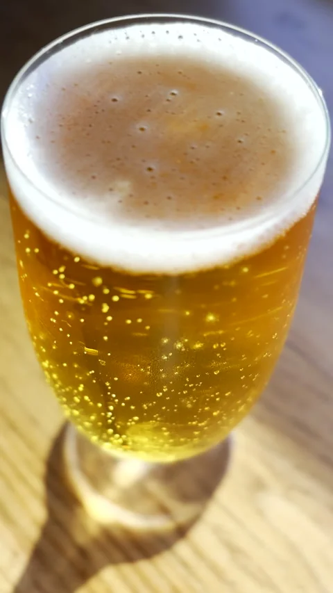 Gas bubbles rise toward foam head of freshly poured beer in tall glass Stock Footage 346082920
