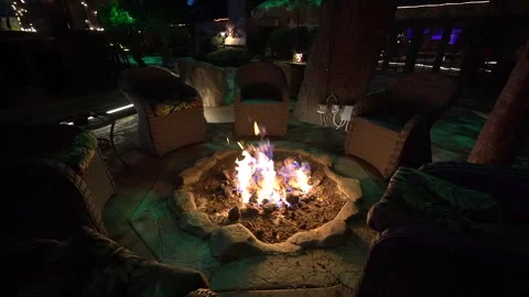 Gas fire pit burning at night surrounded by wicker patio chairs Stock Footage 345540727