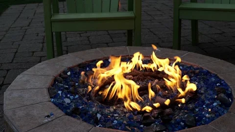 Gas or propane powered circular fire pit with blue rocks and relaxing chairs Stock Footage 201213215