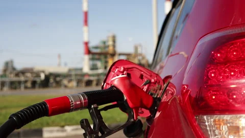 Gas pump nozzle inserted into red car fuel tank at oil refinery background Stock Footage 311060717