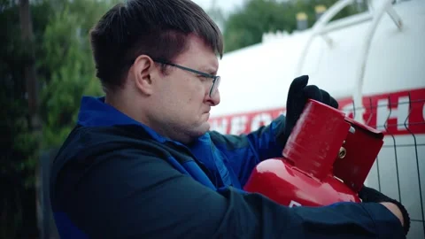 A gas station operator in uniform checks the expiration date of red gas cylinder Video stock 282671021
