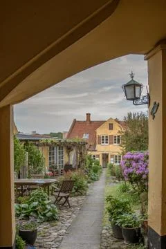 A gateway and a path through a grden full of flowers leading up to a yellow h Stock Photos