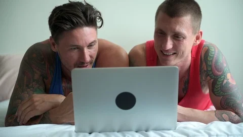 Gay couple in bed using laptop computer. Talking. Stock Footage 105323073