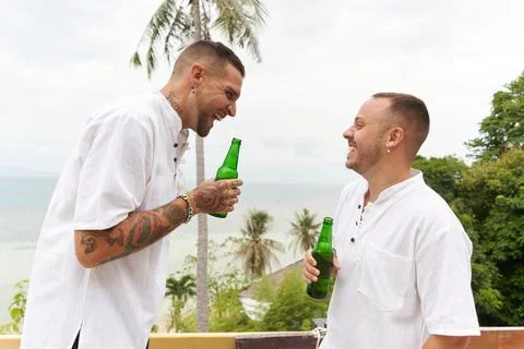Gay couple drinking beer while laughing and talking outdoors Stock Photos