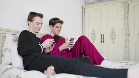 Gay couple relaxing in bed using smartphone and tablet Stock Footage 337883720