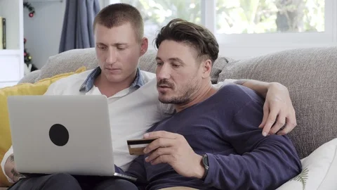 Gay couple relaxing on couch using laptop computer. Online shopping. Stock Footage 105298216