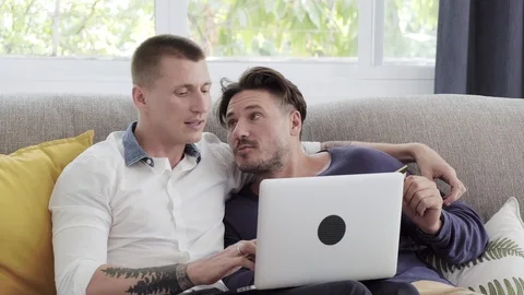 Gay couple relaxing on couch using laptop computer. Thinking and typing. Stock Footage 105298425