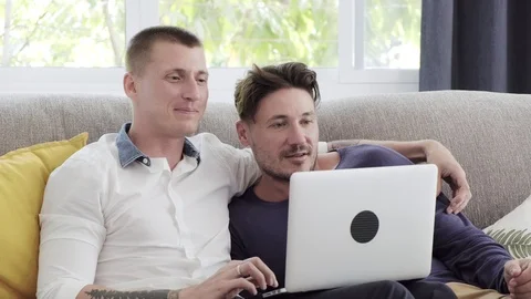 Gay couple relaxing on couch using laptop computer. Try shopping online. Stock Footage 105298436