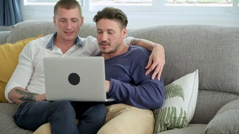 Gay couple relaxing on couch using laptop computer. Completing transaction. Stock Footage 105314341