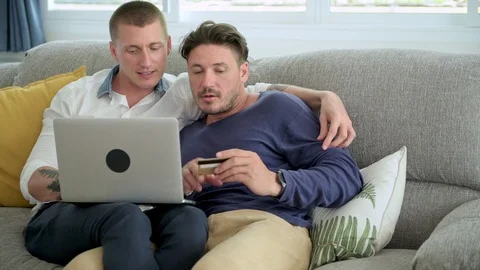 Gay couple relaxing on couch using laptop computer. Looking at credit card. Stock Footage 105314909