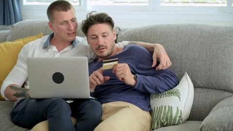 Gay couple relaxing on couch using laptop computer. Telling what to key into Stock Footage 105315167