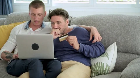 Gay couple relaxing on couch using laptop computer. Try to check the error on Stock Footage 105315541