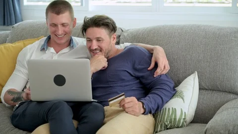 Gay couple relaxing on couch using laptop computer. Talking and holding card. Stock Footage 105315798
