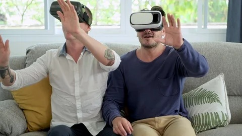 Gay couple relaxing on couch using virtual reality device. Exploring the VR Stock Footage 105316227