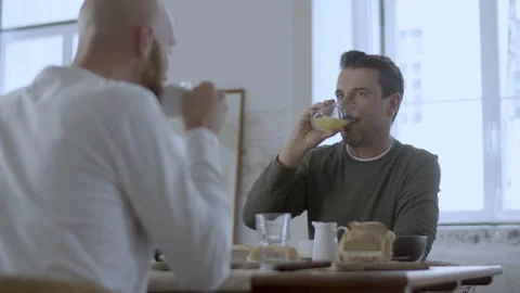 Gay couple sitting at table, having breakfast and talking Stock Footage 229633153