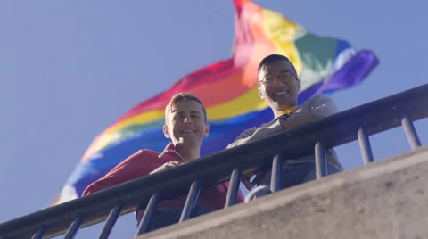 Gay Couple Stand Beneath Gay Pride Flag And Smile Proudly Stock Footage