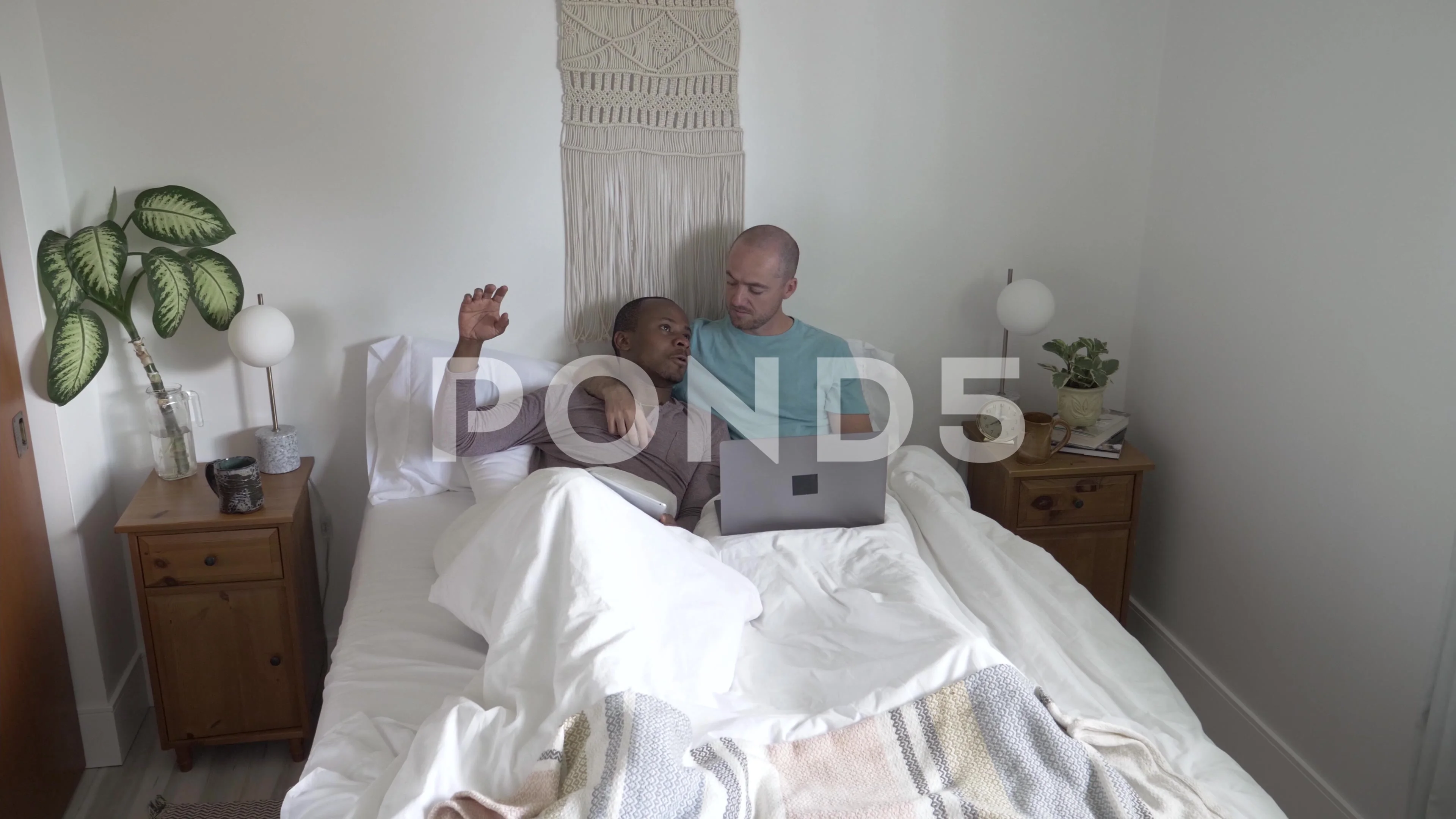 Gay male couple working and talking in bed