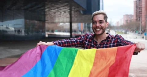 Gay man with makeup on having fun holding lgbt rainbow flag outdoor Stock Footage 175793079