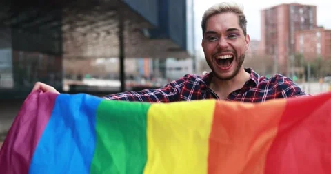 Gay man with makeup on having fun holding lgbt rainbow flag outdoor 動画素材 175793217