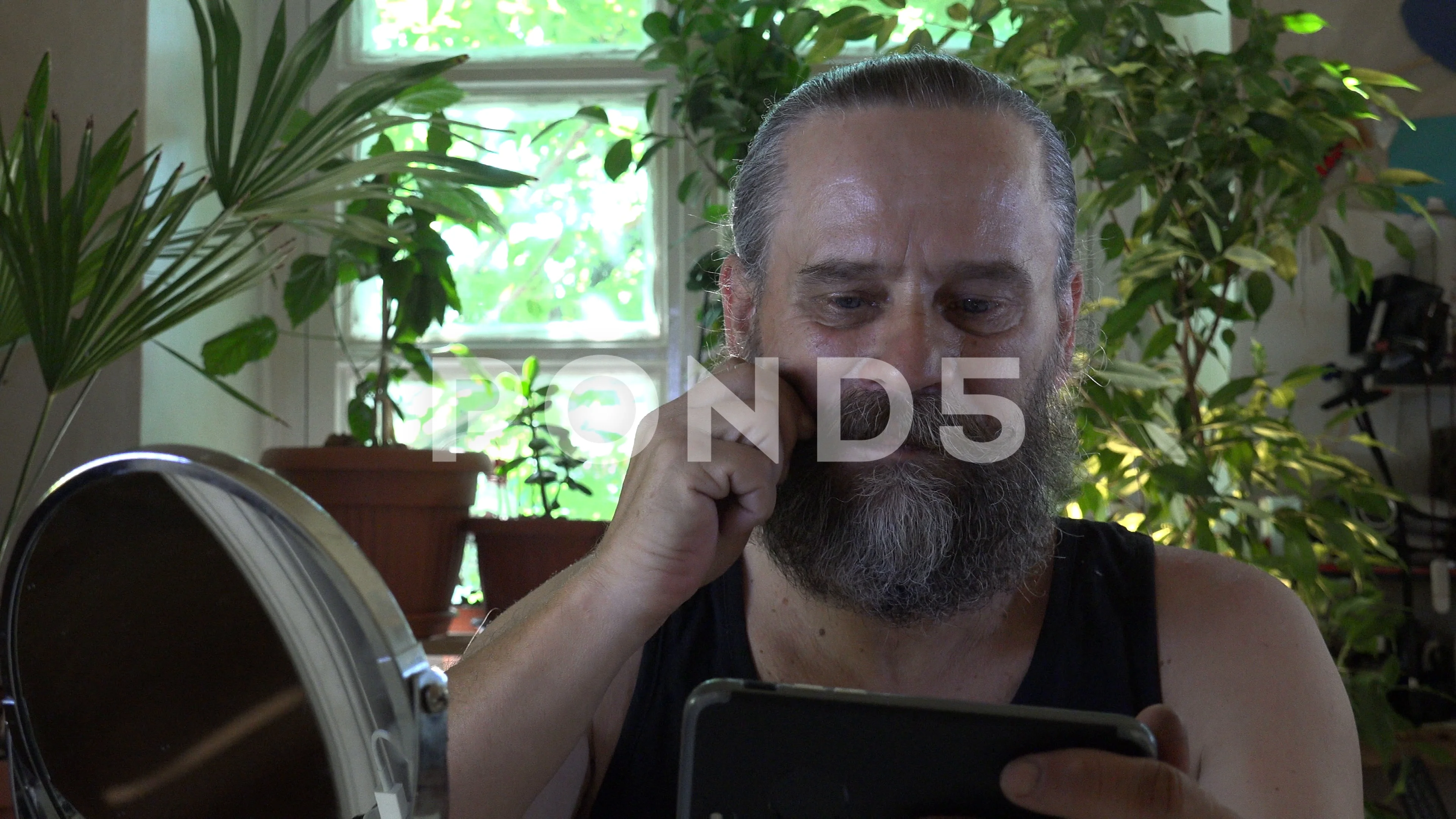 Gay mustache man in room of window and home flowers with mobile phone