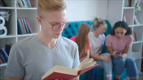 Geek is reading tutorial while teen girls are laughing behind his back Stock Footage 106440105
