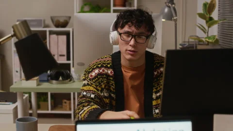Gen Z Guy Singing with Headphones While Working at Office Desk in Evening Stock Footage 327767906